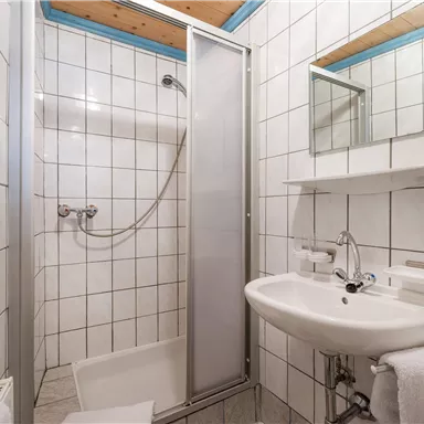 Ein einfaches Badezimmer mit einem Duschbereich und einem Waschbecken. Die Wände sind gefliest und es gibt ein Wandspiegel.