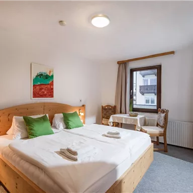 Ein gemütliches Schlafzimmer mit zwei Betten, eleganter Holzmöbel und grünen Kissen. Ein kleiner Tisch mit zwei Stühlen ergänzt die entspannende Atmosphäre.