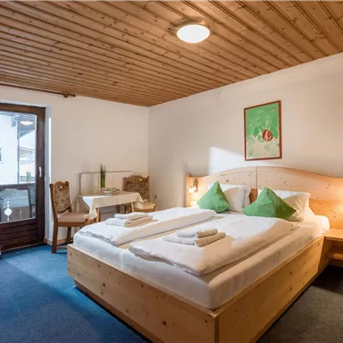 Ein gemütliches Schlafzimmer mit einem Doppelbett und grünen Kissen. Es gibt Holzinterieur und einen kleinen Tisch am Fenster.