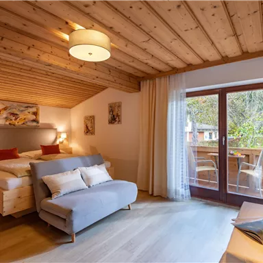 A cozy room with wooden ceilings and a large bed. There is a balcony with a view and a comfortable couch.