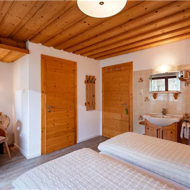 A cozy room with wooden walls and a double bed. There is a table, chairs, and a small bathroom.
