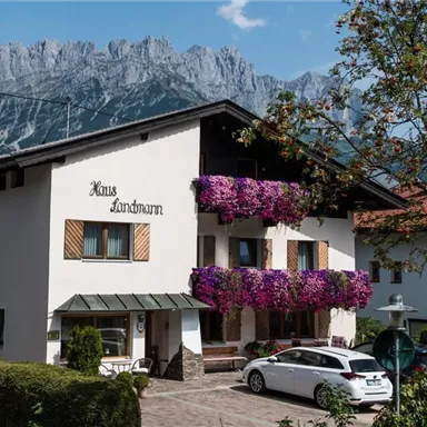Ein charmantes Haus mit bunten Blumenampeln und einer malerischen Berglandschaft im Hintergrund. Es ist einladend und typisch für alpine Regionen.
