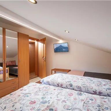 A cozy attic room with two beds and a large wardrobe. A small seating area and a television complete the offer.