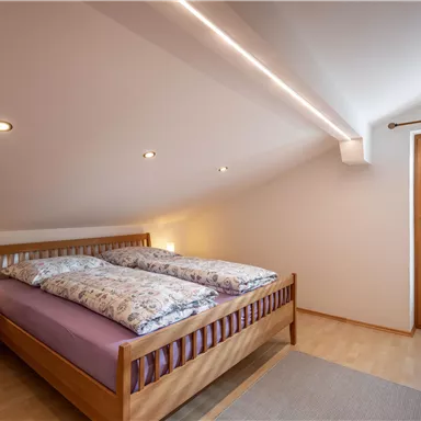 A cozy bedroom with a double bed and light wood flooring. Large windows provide plenty of daylight and a view outside.