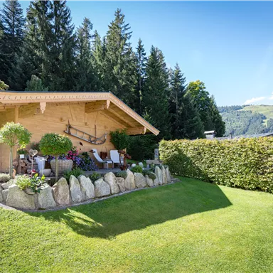 A cozy wooden house surrounded by green trees and well-maintained grass. Blooming plants and a relaxed atmosphere invite you to linger.