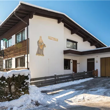 Ein modernes Haus im Schnee mit einem traditionellen Wandbild. Der klare blaue Himmel hebt die winterliche Atmosphäre hervor.