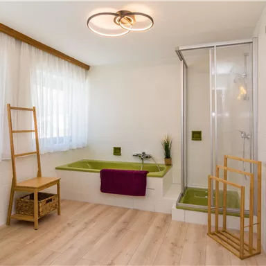 Ein modernes Badezimmer mit einer Duschkabine und einem gemütlichen Badewannenbereich. Der Raum ist hell und freundlich, mit Holz- und Grüntönen gestaltet.