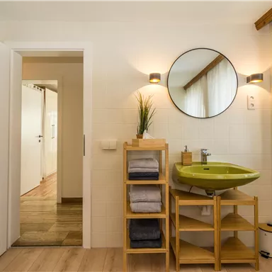 Ein modernes Badezimmer mit einem grünen Waschbecken und einem großen Spiegel. Hintertüren führen zu einem hellen Flur.