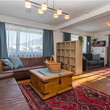 Ein gemütliches Wohnzimmer mit einer braunen Couch und einem Holzkaffetisch. Der Raum hat große Fenster und einen schönen Blick auf die Berge.