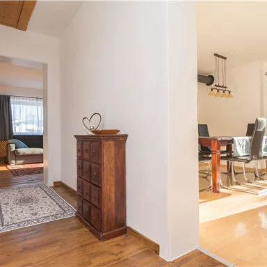 Ein heller Flur mit Holzfußboden und einem kleinen Schrank. Im Hintergrund ist ein Essbereich mit einem großen Tisch und Stühlen sichtbar.