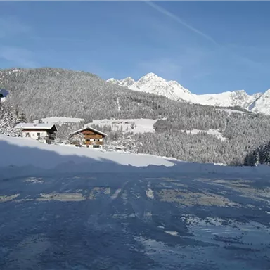 Eine verschneite Landschaft mit schneebedeckten Bergen im Hintergrund. Im Vordergrund sind zwei Hütten sichtbar, umgeben von frisch gefallenem Schnee.