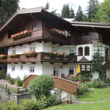 A charming alpine house with balconies and blooming flowers. Surrounded by green countryside and trees.