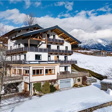 A beautiful, modern house in a snowy landscape. In the background, snow-covered mountains and a blue sky can be seen.
