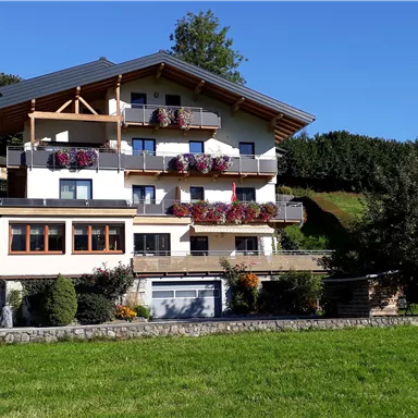 A modern multi-family house with balconies and floral decorations. In the foreground, there is a green meadow.