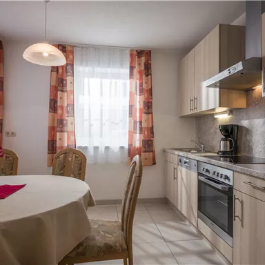 Eine moderne Küche mit einem runden Tisch und hellen Vorhängen. Die Holzschränke und Geräte verleihen dem Raum eine gemütliche Atmosphäre.