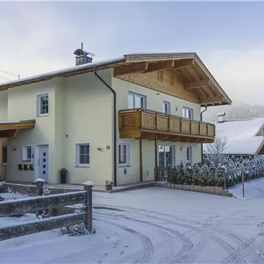 Ein gemütliches Haus im Schnee mit einem modernen Holzdesign. Die Umgebung ist winterlich und friedlich, mit schneebedeckten Bäumen.