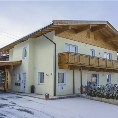 Ein modernes Haus mit einem Holzbalcony in einer verschneiten Umgebung. Der Himmel ist bewölkt, und es ist ruhig und idyllisch.