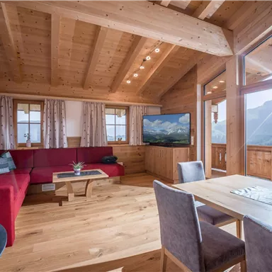 A cozy living room with wood paneling, a red couch, and a large window with a mountain view. The table is set for four people.