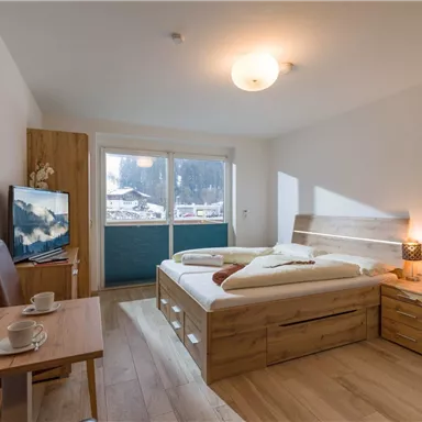 Ein gemütliches Schlafzimmer mit einem großen Doppelbett und hellen Holzmöbeln. Ein Tisch mit zwei Tassen und ein Fernseher sind ebenfalls vorhanden.