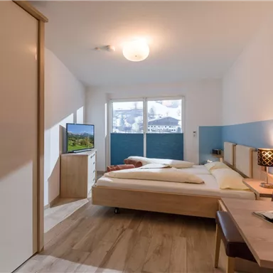 Ein modernes Zimmer mit zwei Betten, einem Fernseher und viel natürlichem Licht. Die Wände sind in sanften Farben gestaltet und der Boden ist aus Holz.