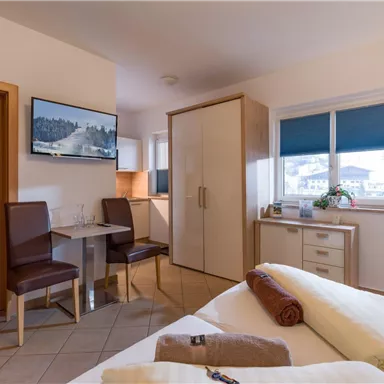 Ein gemütliches Zimmer mit zwei Betten, einem Tisch und zwei Stühlen. Die Fenster bieten einen Blick auf die Umgebung und es gibt einen Fernseher an der Wand.