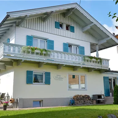 Ein charmantes Haus im alpinen Stil mit blauen Fensterläden. Vor der Haustür befindet sich ein gepflegter Garten.