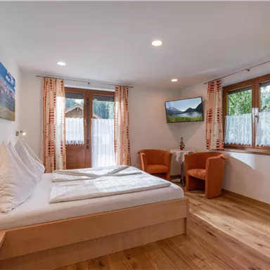 Ein gemütliches Schlafzimmer mit einem Doppelbett und modernen Möbeln. Große Fenster bieten einen Blick auf die Natur und sorgen für viel Tageslicht.