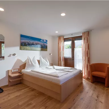 Ein gemütliches Hotelzimmer mit einem Doppelbett, schönem Holzfußboden und einem Fernseher. Große Fenster bieten Licht und den Blick auf die Landschaft.