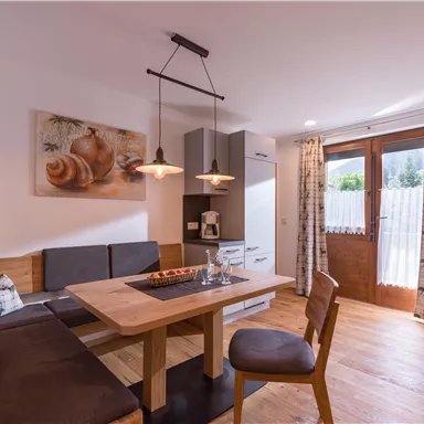 Ein gemütlicher Essbereich mit Holzstühlen und Tisch. Der Raum ist hell und modern, mit einem Fenster und warmem Licht.