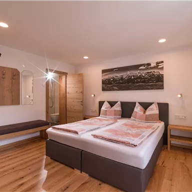 Ein modernes Schlafzimmer mit zwei Betten und Holzfußboden. Es gibt einen Fernseher und eine dekorative Bilderwand.