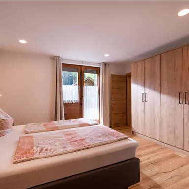 Ein gemütliches Schlafzimmer mit zwei Betten und großen Fenstern. Der Raum hat warme Holztöne und einen Kleiderschrank aus Holz.
