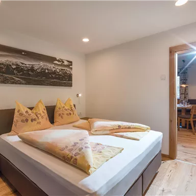 Ein gemütliches Schlafzimmer mit einem Doppelbett und gelben Kissen. Die Holzdecken und der Boden schaffen eine warme Atmosphäre.