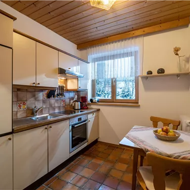 Eine gemütliche Küche mit Holzdecke und modernen Geräten. Am Tisch stehen frisches Obst und eine warme Atmosphäre.