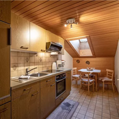 Eine gemütliche Küche mit Holzregalen und modernem Kochgerät. Ein kleiner Tisch mit Stühlen steht neben einem Dachfenster.