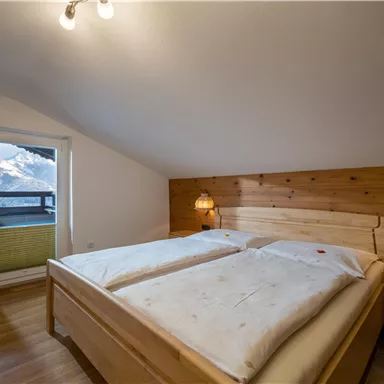 Ein gemütliches Schlafzimmer mit einem Holzbett und zwei Nachttischen. Es hat ein Fenster mit Blick auf die Berge und einen Balkon.