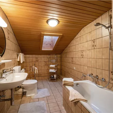 Ein modernes Badezimmer mit Holzbalkendecke und Fliesen. Es verfügt über eine Badewanne, ein Waschbecken und eine Toilette.