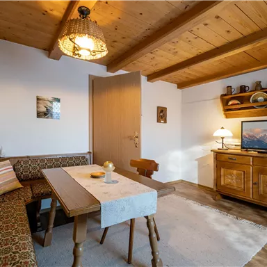 Ein gemütliches Wohnzimmer mit Holzdecke und einem Essbereich. Eine Couch, ein Tisch und ein Fernseher vervollständigen die einladende Atmosphäre.