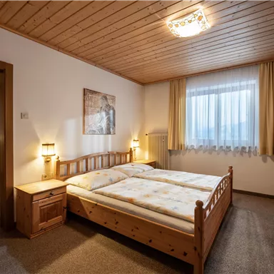 Ein gemütliches Schlafzimmer mit einem großen Doppelbett und Holzmöbeln. Das Zimmer hat große Fenster, die für viel Licht sorgen.