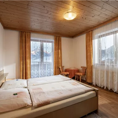 Ein gemütliches Schlafzimmer mit einem Doppelbett und Holzdecken. Große Fenster lassen viel Licht herein und bieten einen schönen Blick nach draußen.