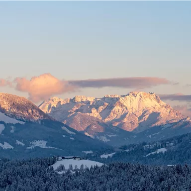 Eine beeindruckende Berglandschaft mit schneebedeckten Gipfeln. Der Himmel ist sanft erleuchtet, während die Sonne aufgeht.
