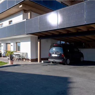 A modern building with a covered parking lot. A car is parked under the carport, surrounded by a well-maintained garden.