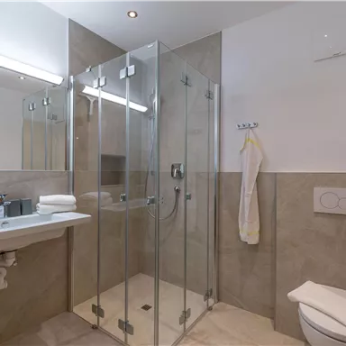 Ein modernes Badezimmer mit einer Glasdusche und hellem Steinboden. Die Wände sind neutral gehalten und es gibt eine elegante Ausstattung.