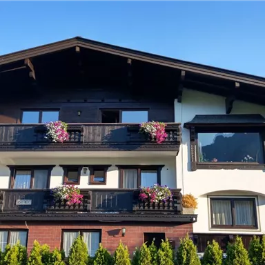 A charming house with balconies, adorned with colorful flowers. In the background, green hills can be seen.