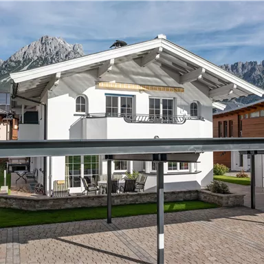 Ein modernes Haus mit weißer Fassade und einem begrünten Grundstück. Im Hintergrund sind majestätische Berge zu sehen.
