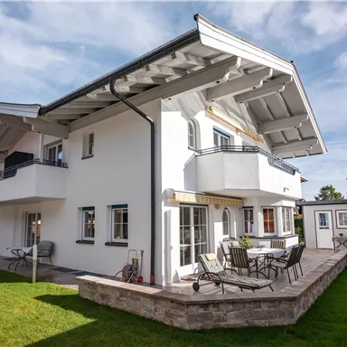 Ein modernes, zweigeschossiges Haus mit einem großzügigen Garten. Die Terrasse ist mit Sitzgelegenheiten ausgestattet und bietet einen Blick auf die Umgebung.