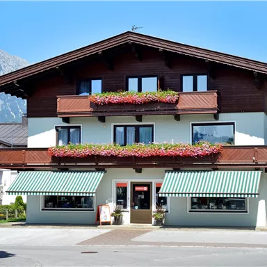 A charming building with wood cladding and colorful flowers on the balcony. In the background, a beautiful mountain landscape can be seen.