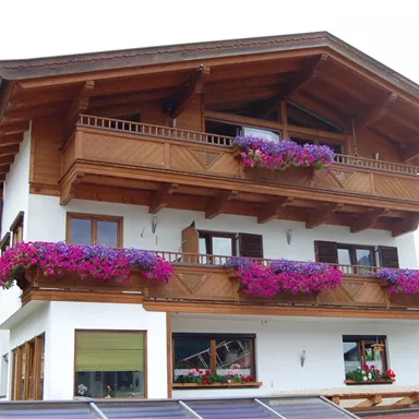 Ein schönes Haus im alpinen Stil mit Holzbalkonen und bunten Blumen. Die Fassade ist hell und freundlich gestaltet.