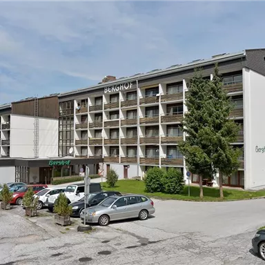 A modern hotel building in a quiet environment. Several cars and plants are in front of the hotel.