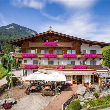 Ein charmantes Hotel mit blühenden Balkonen und einer einladenden Terrasse. Umgeben von malerischen Bergen und einer grünen Landschaft.