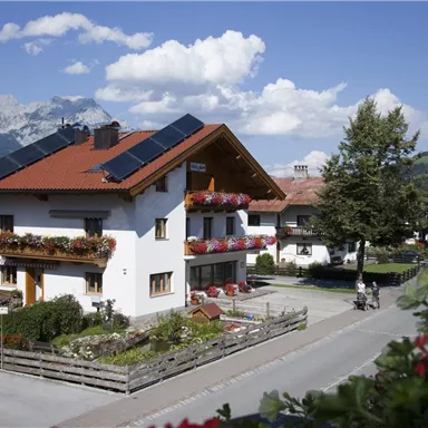 Ein schönes Haus mit Blumenkästen und Solarpaneelen. Im Hintergrund sind Berge und ein klarer Himmel sichtbar.
